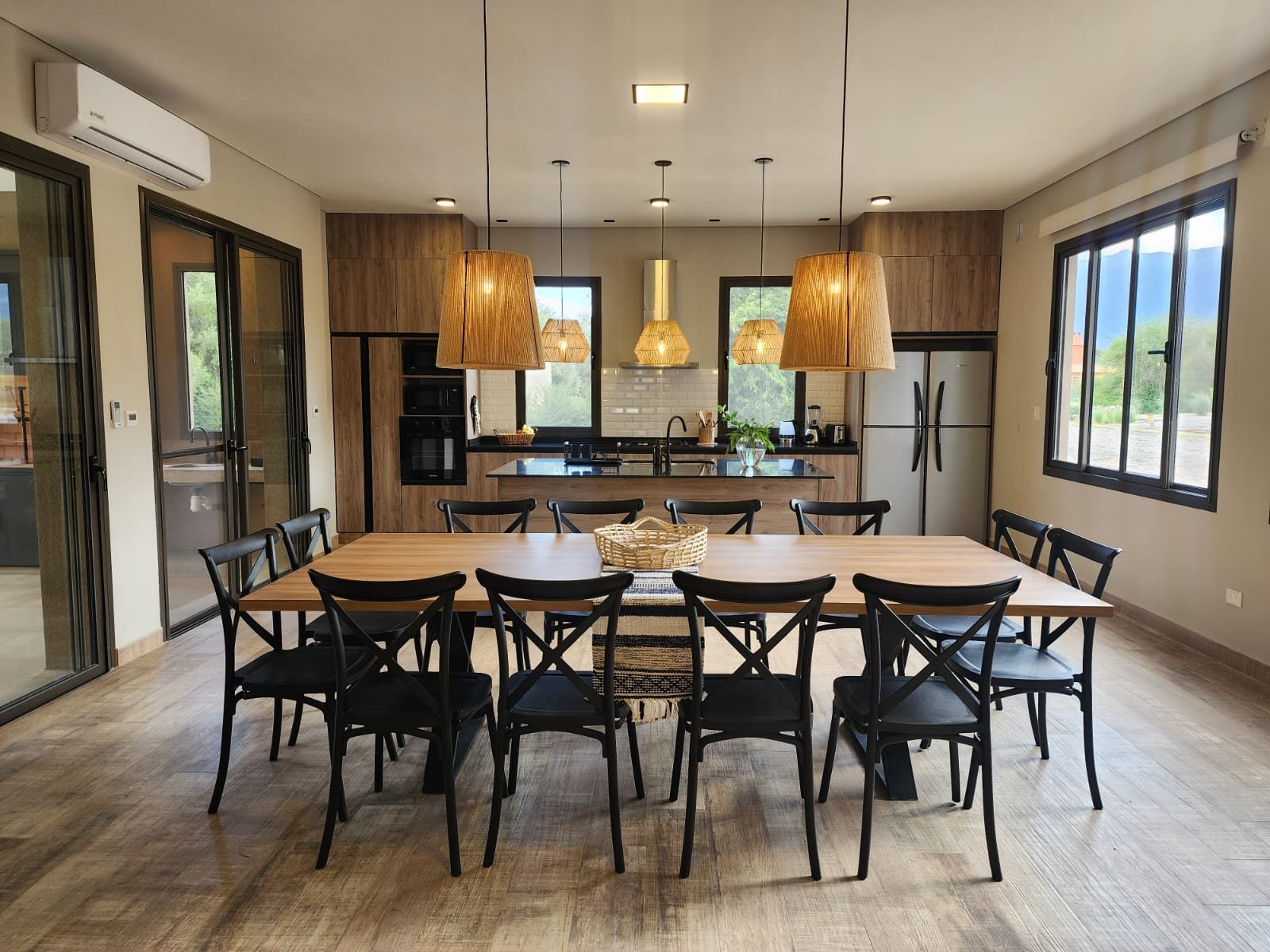 Sala de jantar e cozinha modernas com mesa de madeira grande e luminárias pendentes tecidas — projeto Ca La Estancia, por Luciana González Anderson, em Cafayate